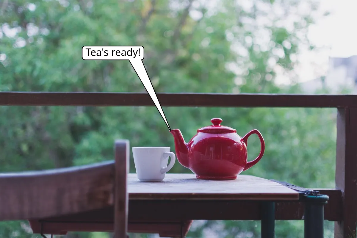 A red teapot and a white mug on a table, with a speech bubble saying Tea's ready! that points at the spout.