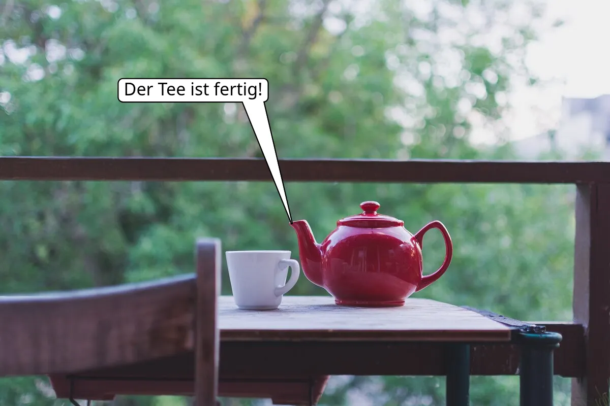 Eine rote Teekanne und ein weißer Becher auf einem Tisch, dazu eine Sprechblase mit „Der Tee ist fertig!“, die auf die Tülle der Kanne zeigt.
